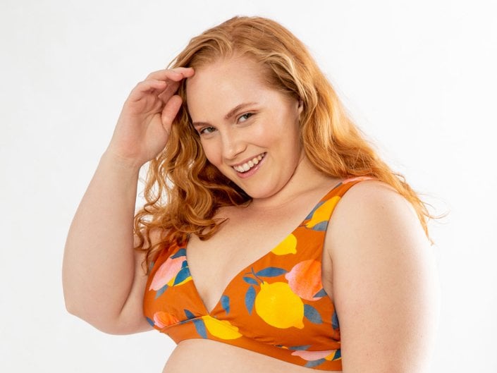 person with red hair smiling and posing with hand resting at hairline