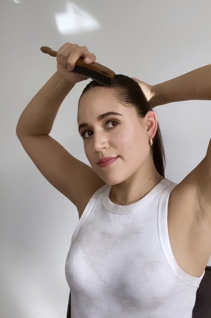 person brushing hair into ponytail