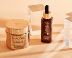 Lancôme Absolu Cream and L’Oréal Paris Facial Tanning Drops photographed on a peach background. 