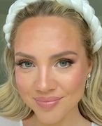 A bride with blonde hair pushed back with a thick white headband wearing natural makeup with pink blush and lipstick