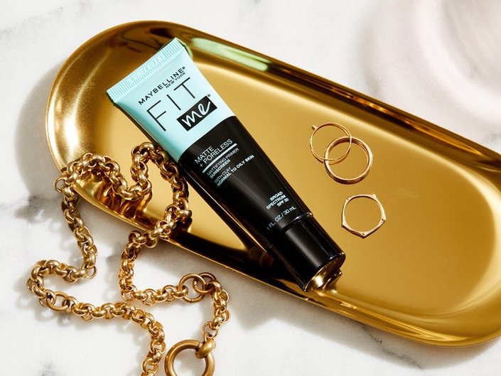 The Maybelline New York Fit Me Matte+ Poreless Mattifying Face Primer lying in a gold tray with rings and a necklace