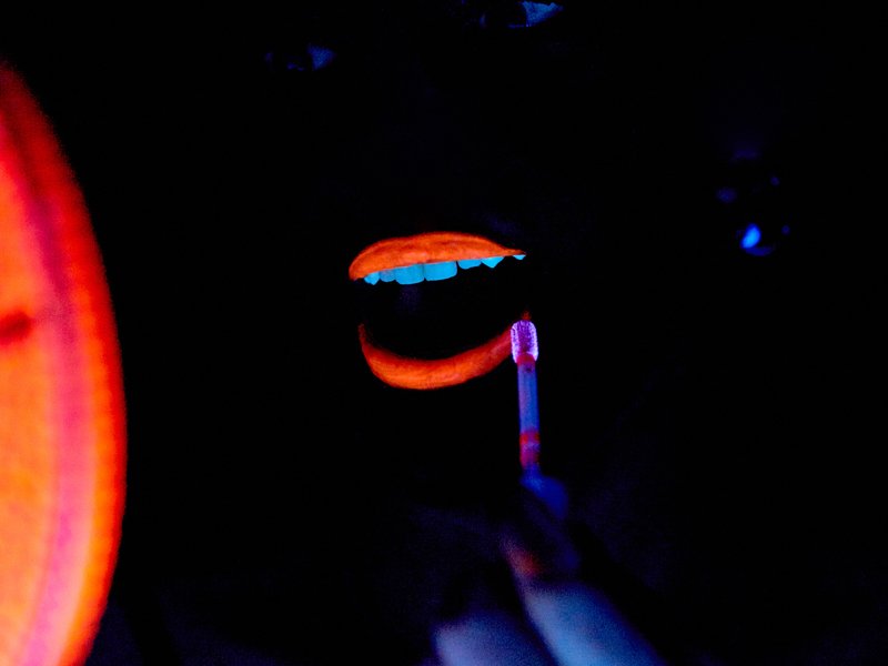 person applying neon orange liquid lipstick in the dark