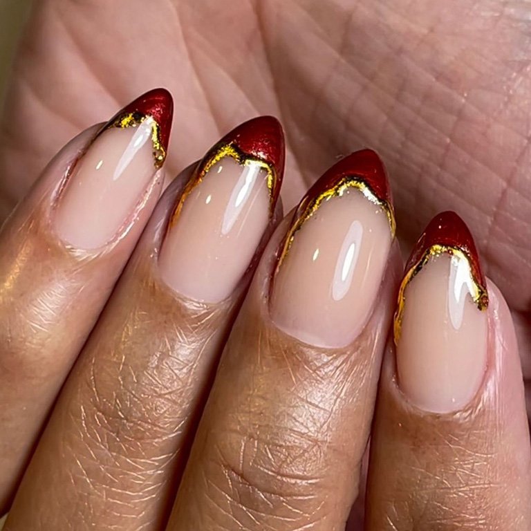 hand with red french tips with gold accents on nails