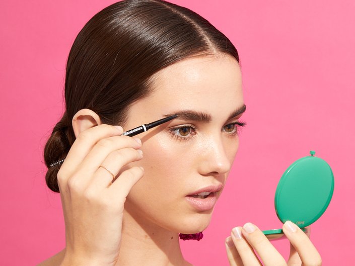 person applying makeup to eyebrow while looking in a compact mirror