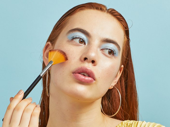 person wearing light blue eyeshadow and holding highlighter brush to cheek