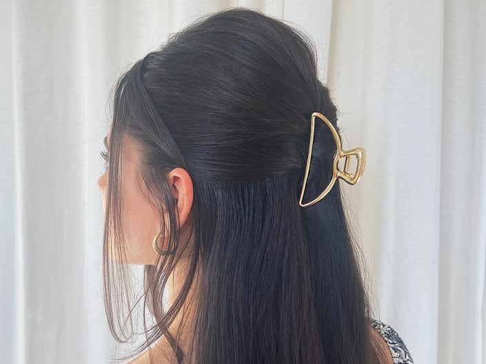 Back of a person’s head with dark hair pulled back with a gold claw clip in a half-up, half-down style