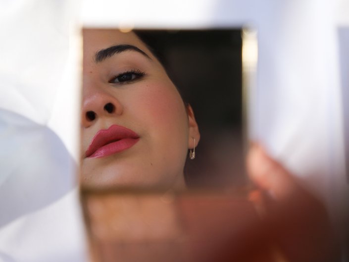 person wearing pink lipstick and looking at reflection through handheld mirror