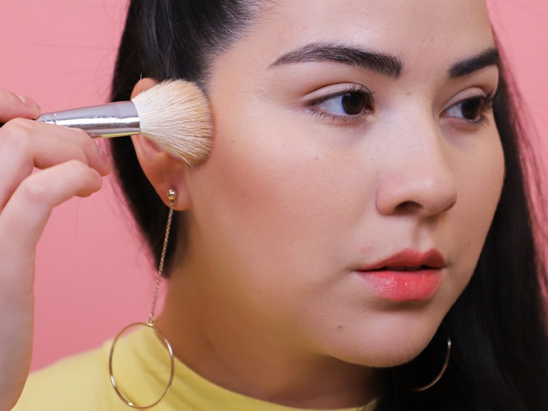 person applying blush to cheek with makeup brush