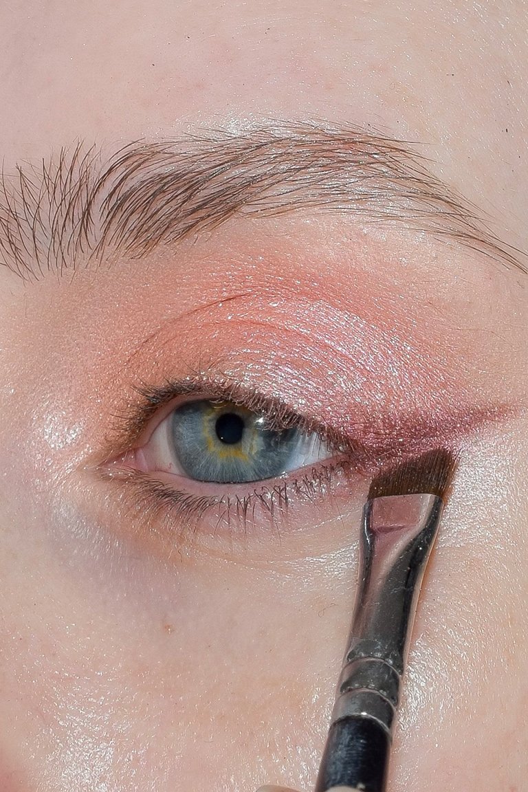 makeup brush applying rose-colored glitter eyeshadow to crease of eye