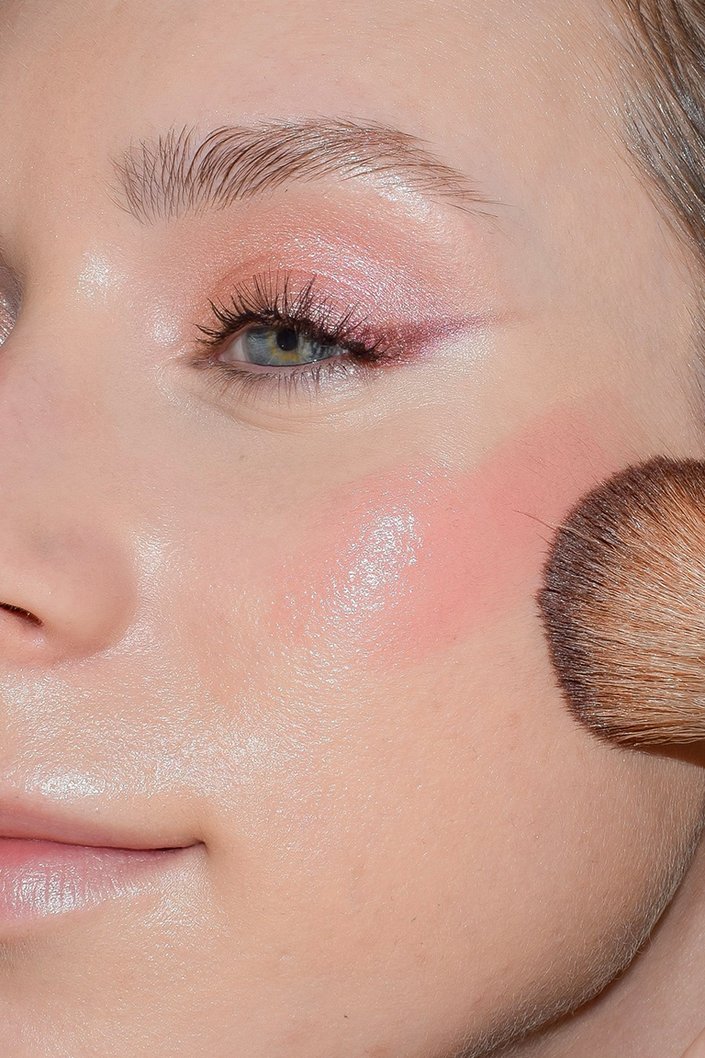 makeup brush applying rose-colored blush to cheek