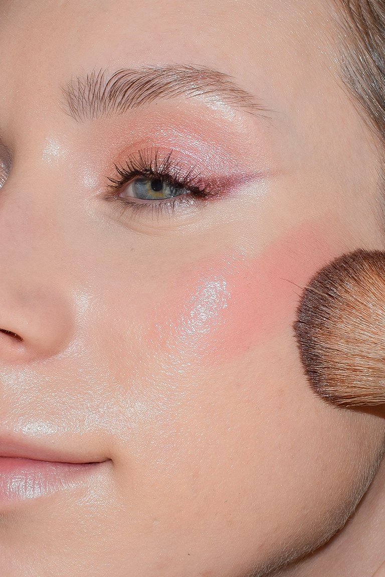 makeup brush applying rose-colored blush to cheek