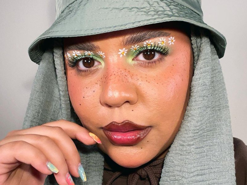 person wearing green eyeshadow with daisies painted under eyebrows
