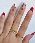 A picture of a hand with a red-and-white French tip and cherry-printed manicure against a white wall