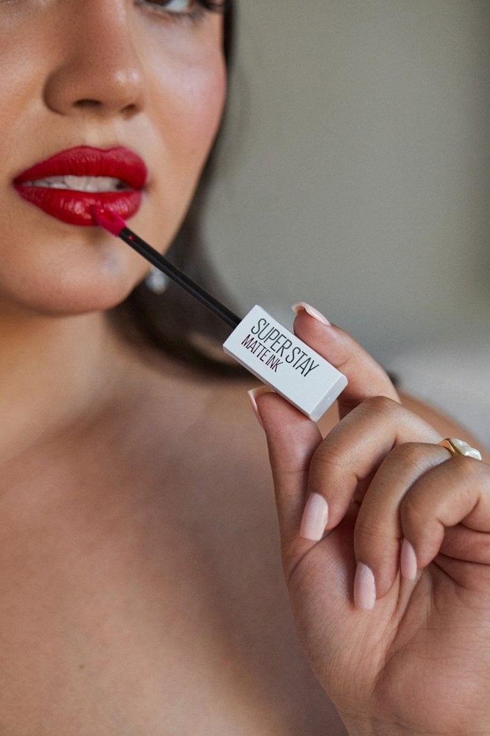 person applying red liquid lipstick to lips