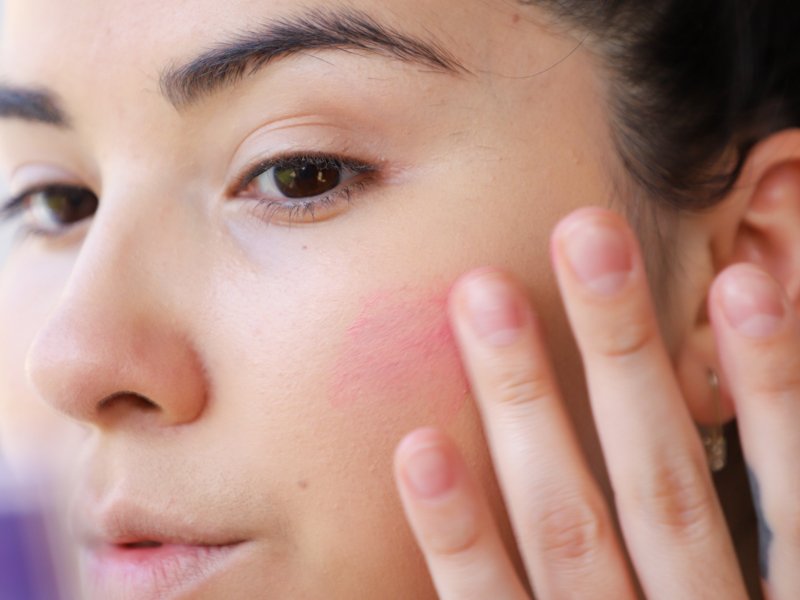 person applying blush to cheek with finger