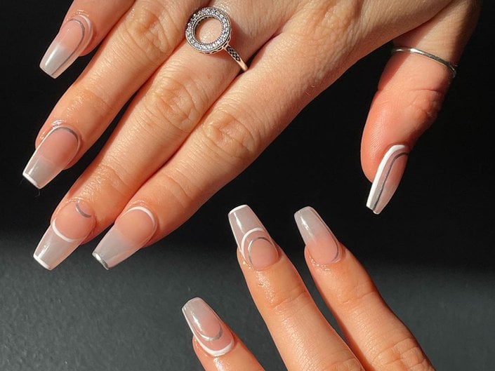 Hands with tapered square nails painted with a negative space manicure with metallic silver accents