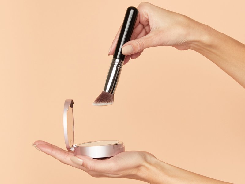 hands holding makeup brush to powder compact
