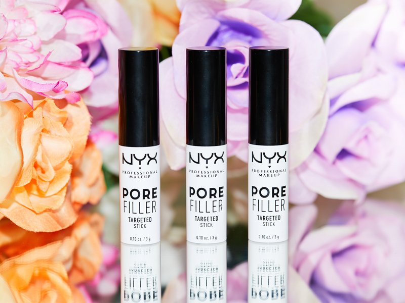 An image of three of the NYX Professional Makeup Pore Filler Targeted Stick against a background of purple and orange flowers