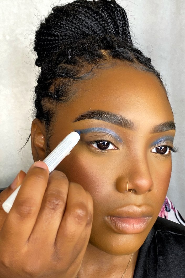 person applying blue eyeshadow stick to eyelid crease