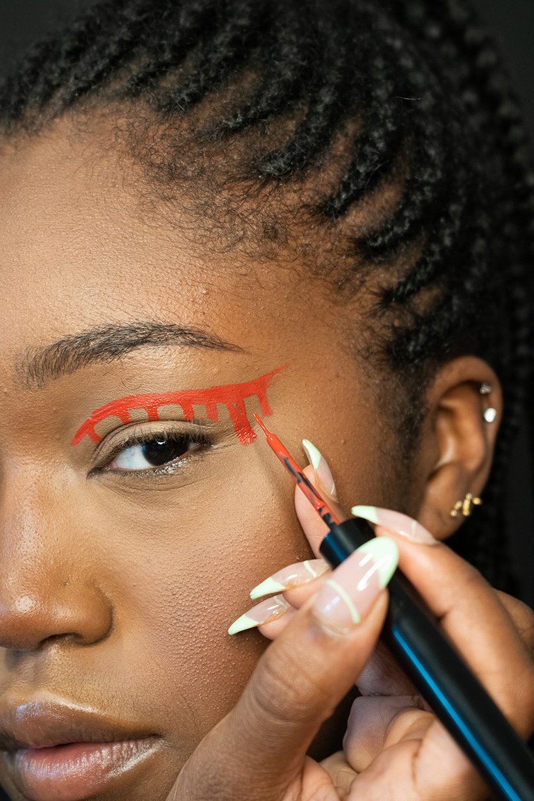 person applying red liquid eyeliner to eyelid