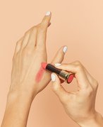 Photo of a person with white painted nails swatching lipstick on their hand