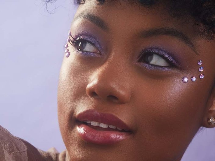 person wearing purple eyeshadow with purple rhinestones on side of eyes