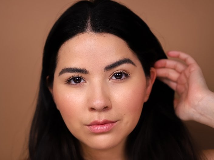 person with dark hair tucking hair behind their ear