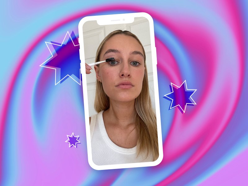 Selfie of editor using a spoolie brush dipped in petroleum jelly to comb her eyelashes, against a pink and purple swirled background with star design