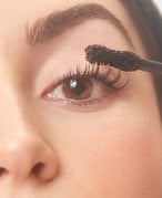 Close-up photo of a model applying black mascara to her top lashes