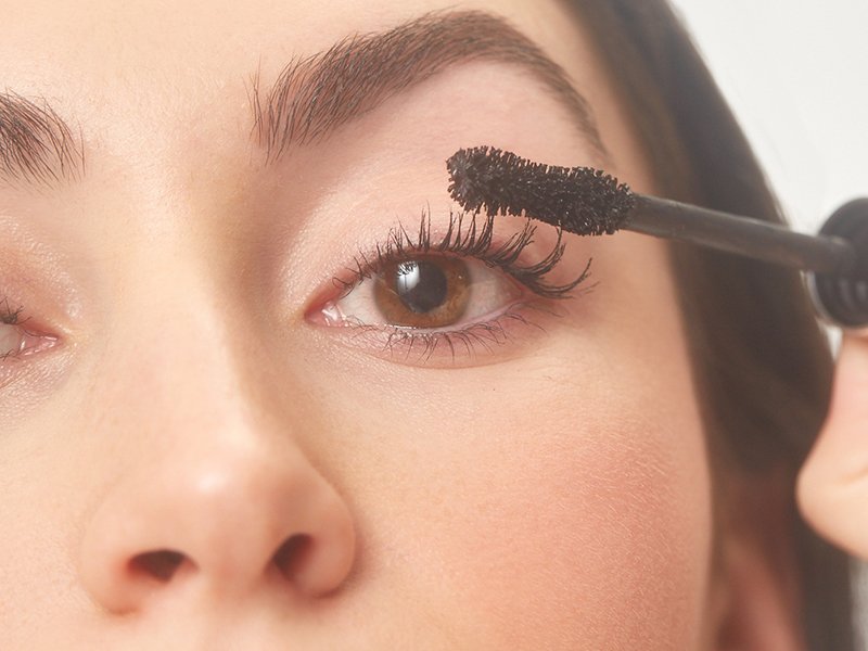 Close-up photo of a model applying black mascara to her top lashes