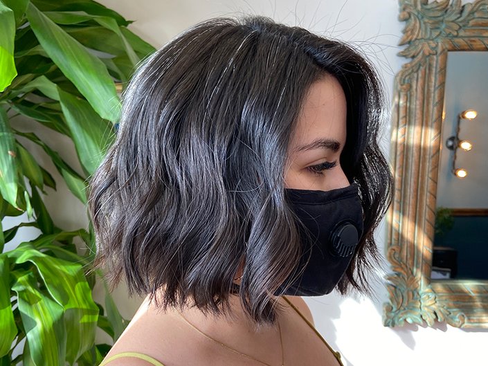 Person wearing a black face mask and facing the side with black hair cut into a wavy blunt bob