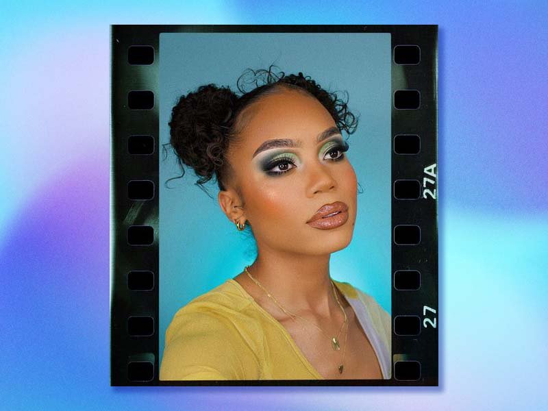 person looking off to the side of the camera wearing green eyeshadow and nude lipstick on a blue background