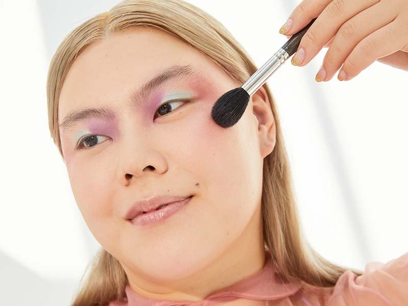 Person applying pink blush with a brush