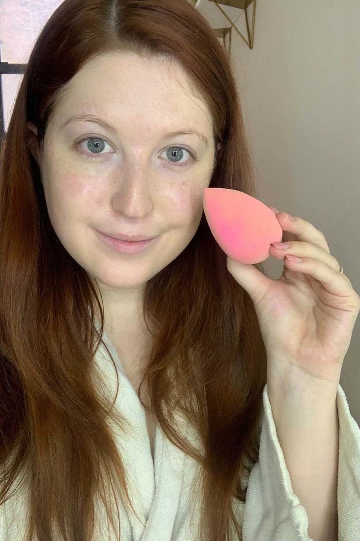 person holding pink beauty blender next to face