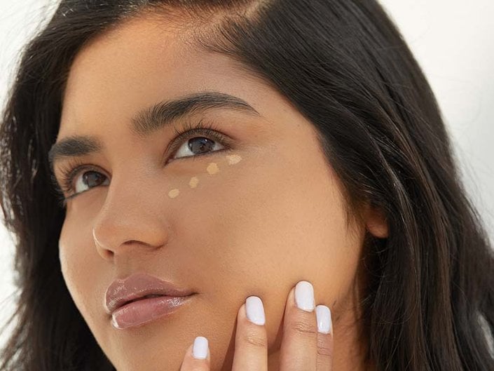 Person with long dark hair with foundation swatched under their eye in small dots