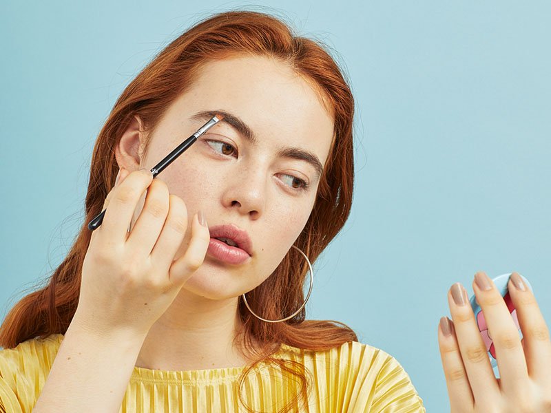 person applying makeup to eyebrow through compact mirror