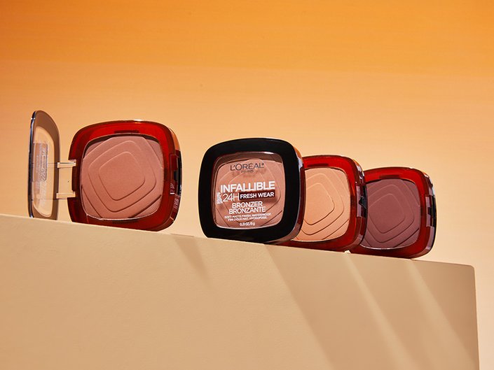 Four different shades of the L'Oréal Paris Infallible Up to 24H Fresh Wear Soft Matte Bronzer lined up against an orange background.