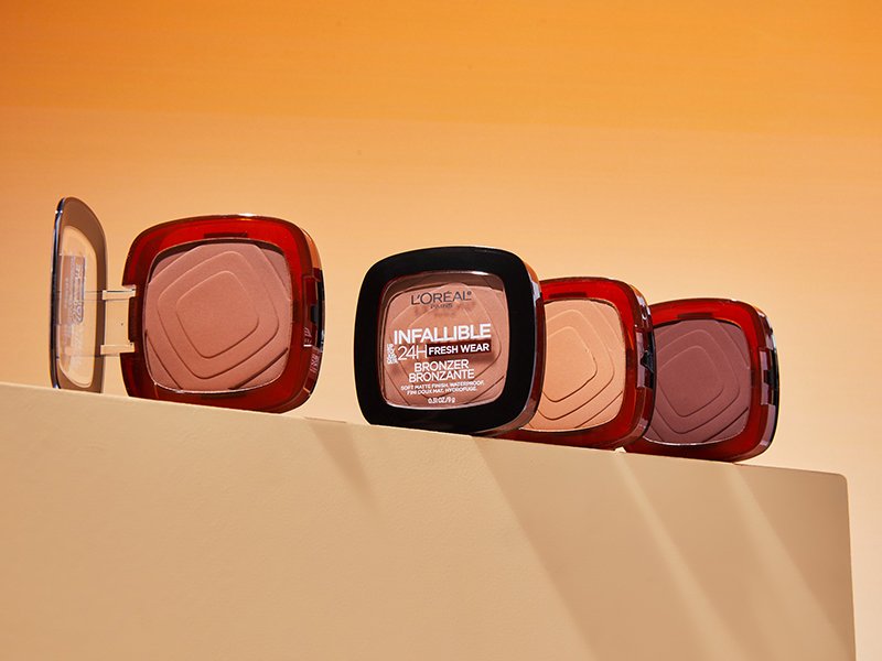 Four different shades of the L'Oréal Paris Infallible Up to 24H Fresh Wear Soft Matte Bronzer lined up against an orange background. 