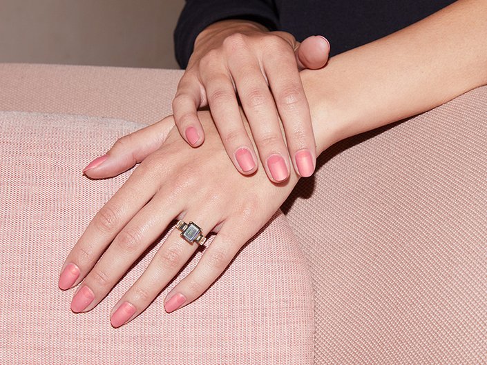 Close-up of hands with a light pink manicure and a ring on one ring finger. One hand is resting on top of the other.