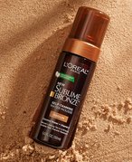 Overhead shot of the L’Oréal Paris Sublime Bronze Self-Tanning Water Mousse lying in the sand