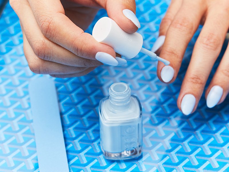 Person painting their nails with a light blue Essie nail polish