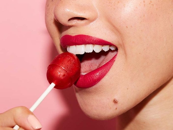 person wearing red lipstick holding red lollipop to mouth