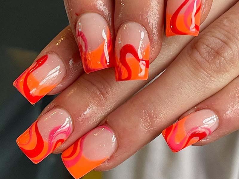 hands with orange, pink, and red lava nail art on nails