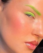 Person staring at the camera, wearing neon green eyeshadow and neon green eyelashes. 