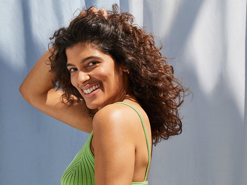Smiling person with green shirt and curly brown hair on white background 