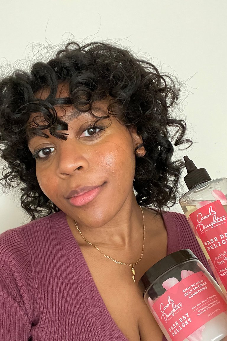 Kat with styled hair holding Carol’s Daughter Wash Day Delight Jelly to Cream Conditioner and Carol's Daughter Wash Day Rose Shampoo
