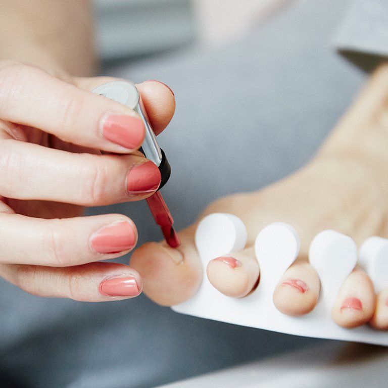 Image of a model painting her toenails with coral nail polish