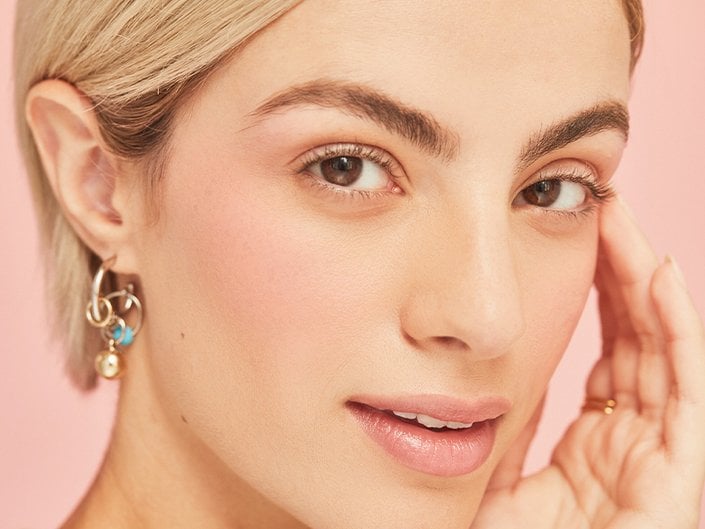 person with soap brows touching face on a pink background