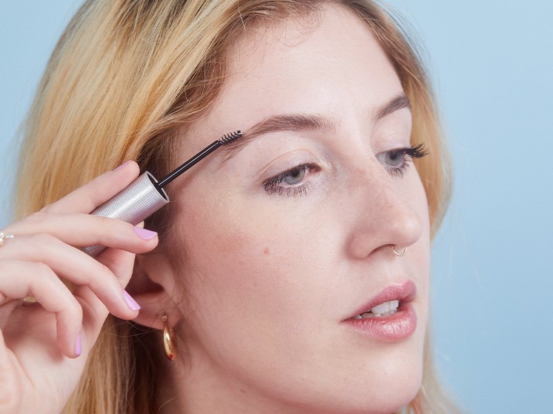 photo of person using eyebrow brush on blue background