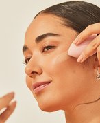 Photo of a young person using a makeup blending sponge to apply foundation while looking into a compact mirror.